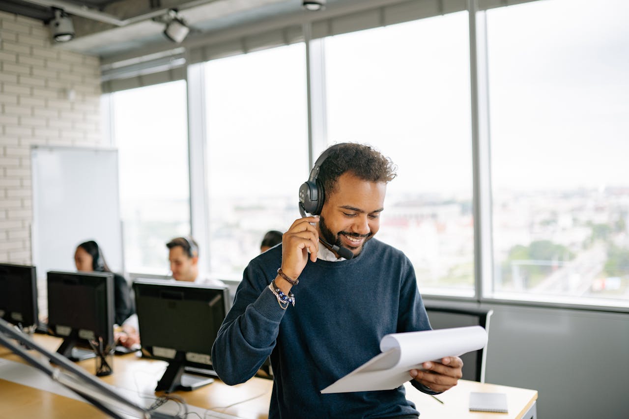 Friendly call center agent engaged in conversation while reviewing documents at his desk.